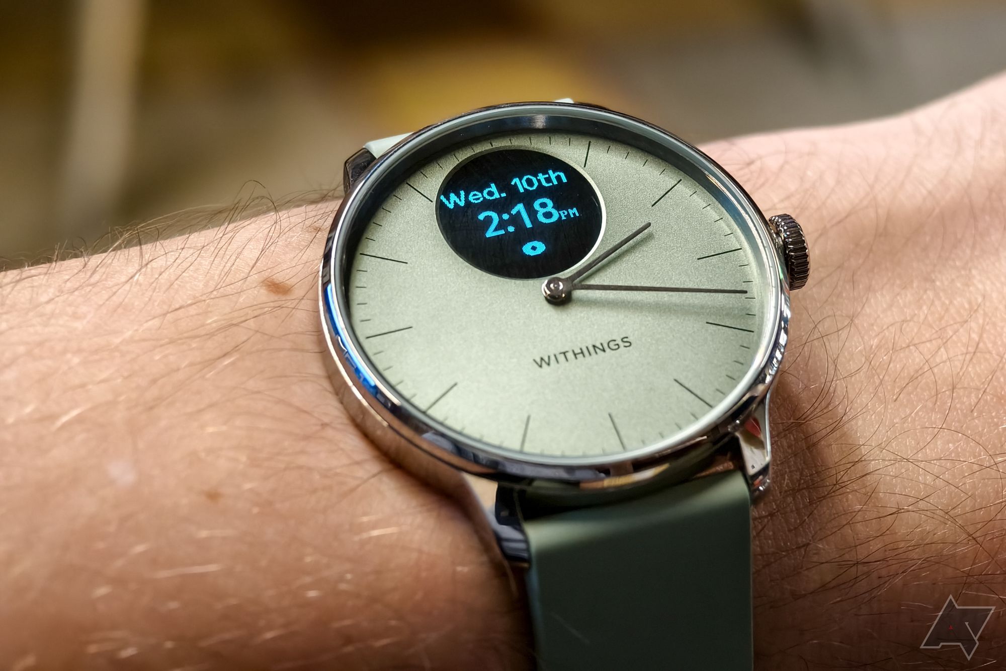 Withings ScanWatch Light in Green, with the display on, photographed on a man's wrist with a close-up on the watch face showing the time