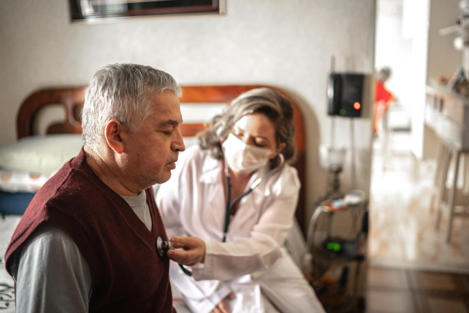 A visiting nurse uses a digital tablet and talks to an elderly man during a home visit